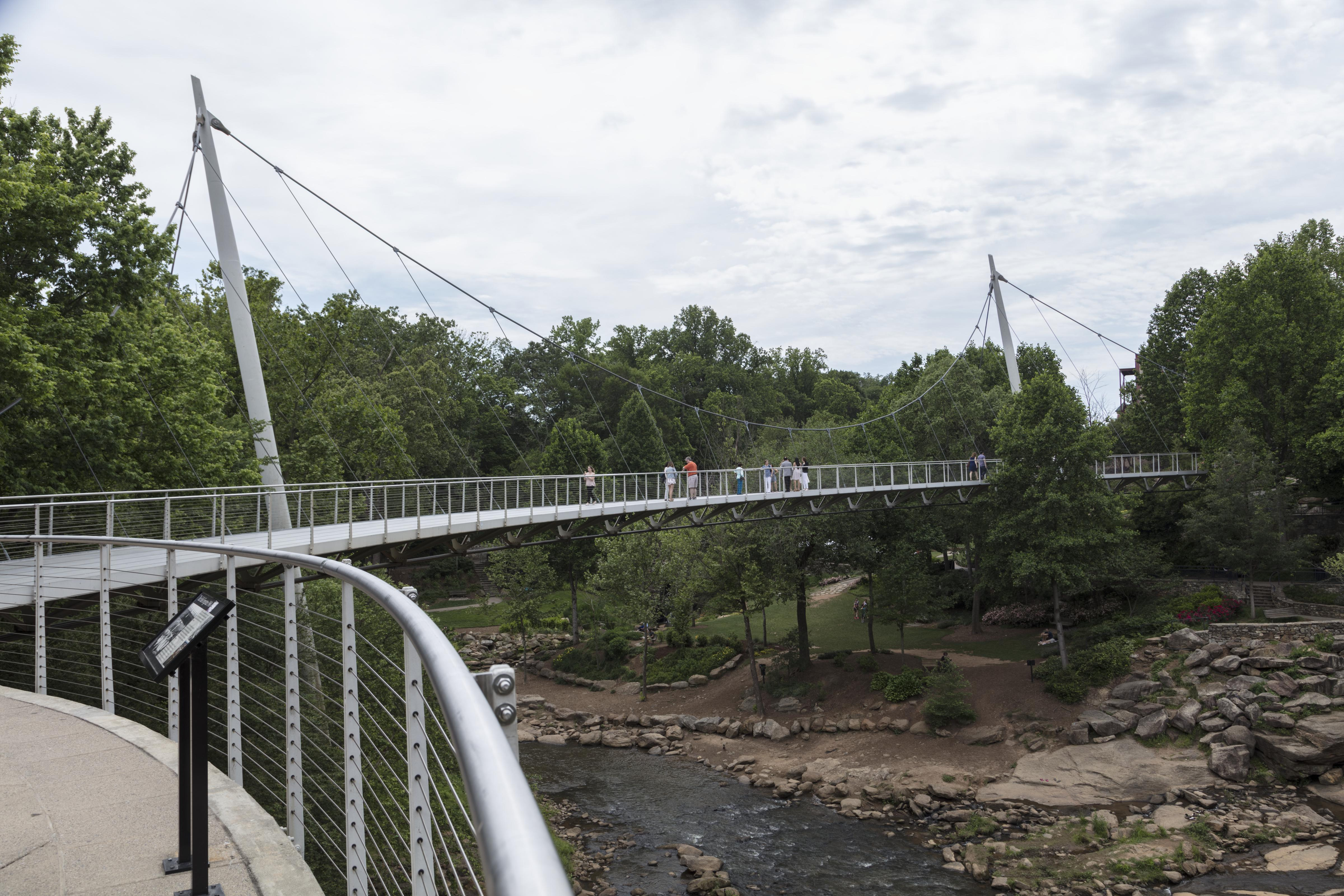 The Liberty Bridge spanning a forested river gorge, suspended from its cables